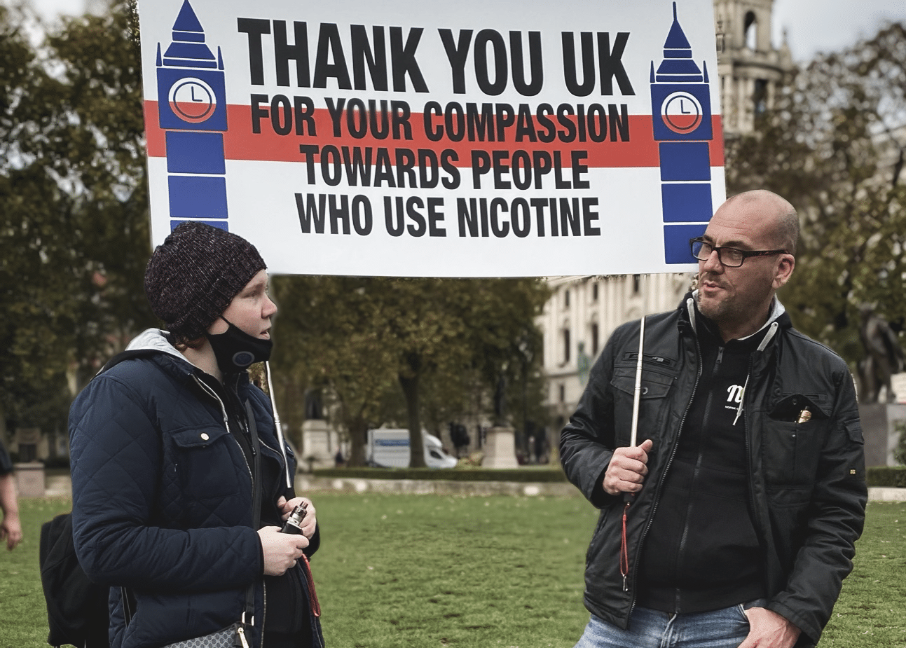 Two people in a park, holding up a banner that reads "Thank you UK for your compassion towards people who use nicotine"